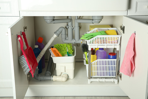 Different cleaning tools and supplies in open cabinet under sink
