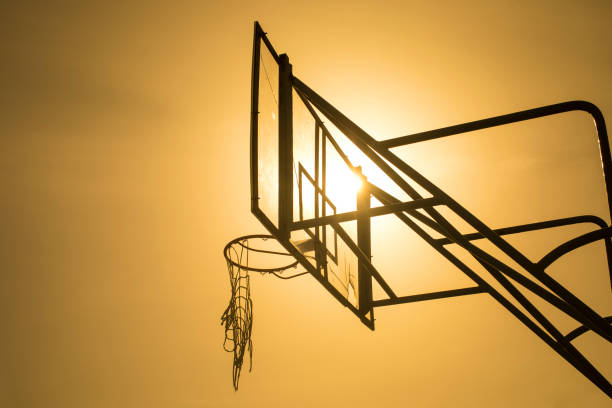 vecchio tabellone da basket in un parco con canestro da basket e vecchia rete rotta appesa al canestro contro il cielo del tramonto. sport e ricreazione. fotografia retroilluminata del tabellone da basket - basketball slam dunk basketball hoop sport foto e immagini stock