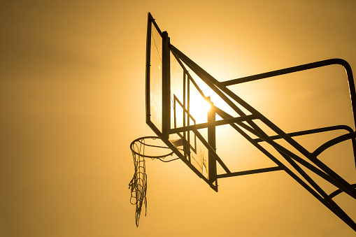 Old basketball backboard in a park with basketball hoop and broken old net hanging from the hoop against sunset sky. Sports and Recreation. backlight photography of basketball backboard