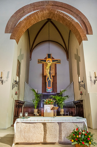 The Altar of a catholic church, in a clean design with some green plants and a bouquet of yellow flowers in front of the altar table. There is a wooden crucifix on the wall.