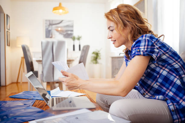 Woman paying bills and working online stock photo Smiling glad woman paying bills online at home while sitting in living room, doing paper work and using laptop computer at her workplace wearing casual clothes personal loan stock pictures, royalty-free photos & images