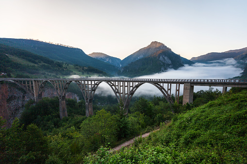 Low clouds under the beautiful bridge over the Tara river canyon at mountains of Durmitor National park in the morning. Tara river canyon is second largest canyon in the world (after Grand Canyon)