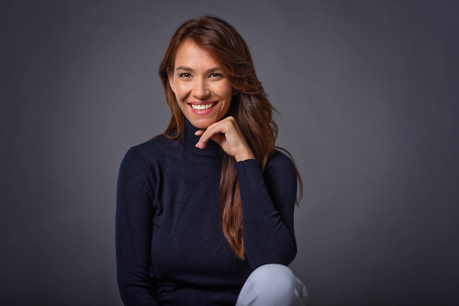 Beautiful smiling woman with white teeth sitting at isolated grey background. Happy woman wearing turtleneck sweater. Copy space.