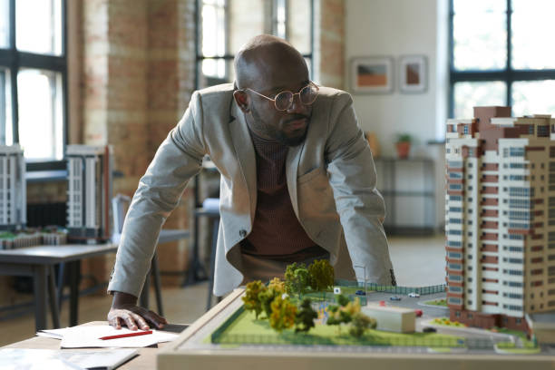 Architect developing new residential area African serious architect in eyeglasses looking at construction model of new residential area during his work at office architect stock pictures, royalty-free photos & images