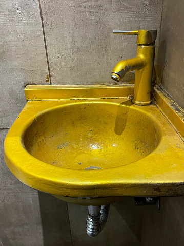 An old rusty bathtub with a metal drain hole. Dirty cracked unclean surface of the bath or sink with red rust stain, close-up. Corrosion, unsanitary concept.