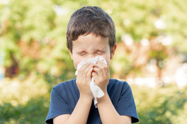 Allergic child sneezing covering nose Allergic child sneezing covering nose with wipe in a park in spring or summer season sneezing photos stock pictures, royalty-free photos & images