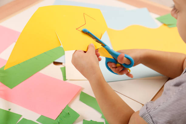 bambina che taglia la carta colorata con le forbici al tavolo, primo piano - brilliant cut foto e immagini stock