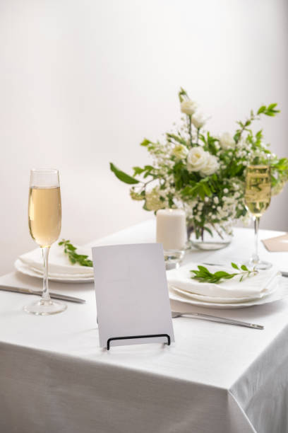 istock Mockup white blank space card for table number or menu. Wedding teble decoration with white flowers, glasses and white napkins. Elegantly decorated table at a wedding reception. Festive table setting. The wedding decor. 1405406646