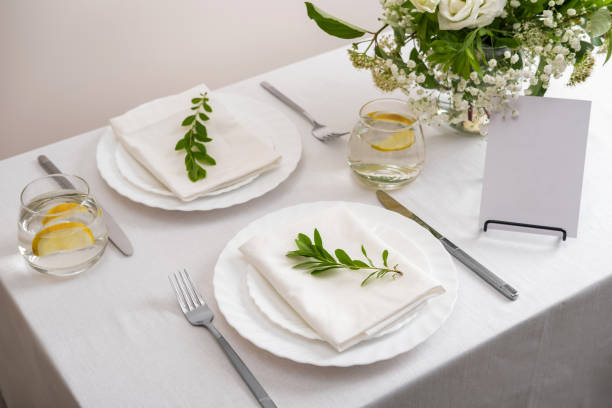 istock Mockup white blank space card for table number or menu. Wedding teble decoration with white flowers, glasses and white napkins. Elegantly decorated table at a wedding reception. Festive table setting. The wedding decor. 1405406693