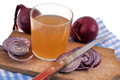 Glass of red onion juice and its ingredients on a cutting board close-up on a white background