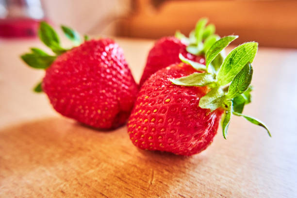 Fresh strawberries lit by the sun lie on a wooden table