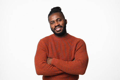 Smiling african-american young man in red sweater with dreadlocks looking at camera with arms crossed isolated in white background