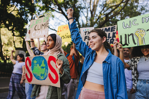 Generation z standing up against climate change. Group of multicultural youth activists carrying posters while marching against global warming. Diverse young people joining the global climate strike.