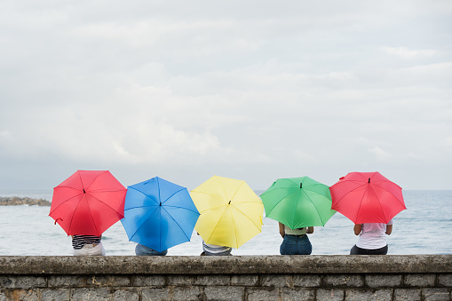 Rear view of people looking at sea in a rainy day. Colorful umbrellas at seaside