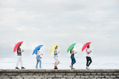Group of teenagers walking on a wall and holding colorful umbrellas. Copy space in the sky.