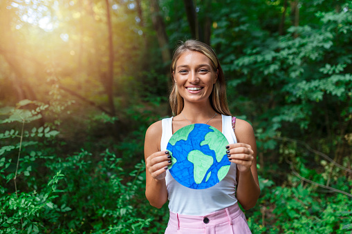 Woman activist holding planet earth poster in woods, environmental pollution concept.