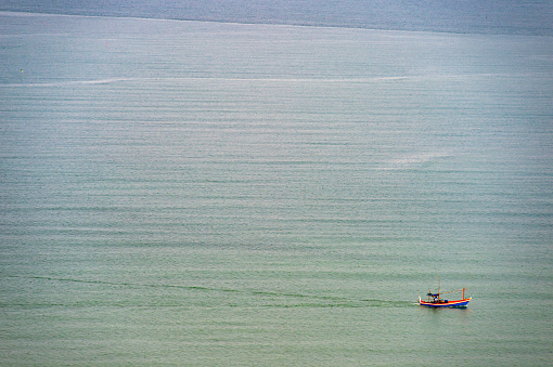 A fisherman rides a motor boat in the sea in the distance. In the water overlooking the view from above, Thailand