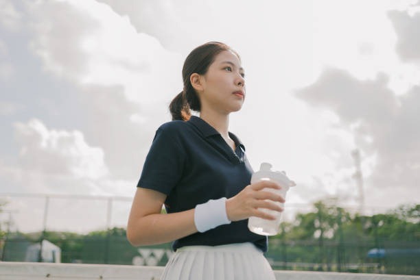 Asian young woman tennis player drinking water and  taking a break during a practice.