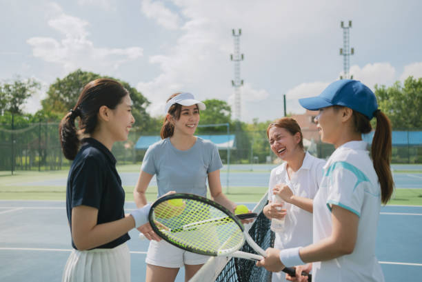 明るい晴れた日に屋外テニスコートで試合後に話したり休んだりする幸せなアジアの若い友情。 - racket sport 写真 ストックフォトと画像