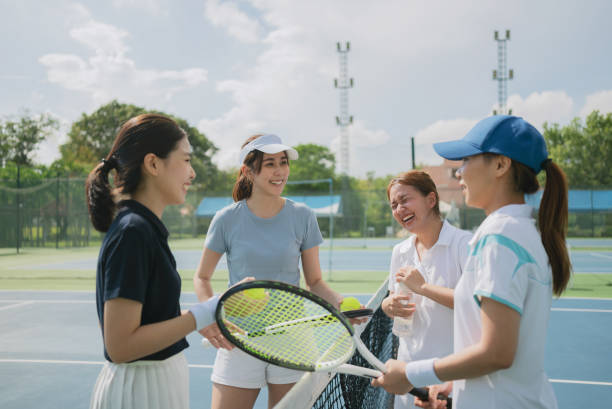 Happy asian young friendship talking and resting after match on the outdoor tennis court on a bright sunny day. stock photo