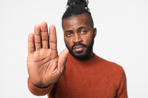 Closeup african-american young man in casual clothes with dreadlocks showing stop gesture with arm palm isolated in white background. Prohibited, not allowed, no pass