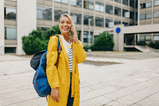 A young Caucasian woman in a yellow raincoat is talking on her cellphone with a big smile.
