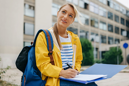 A young Caucasian woman is wearing a bright yellow raincoat and writing on a piece of paper.