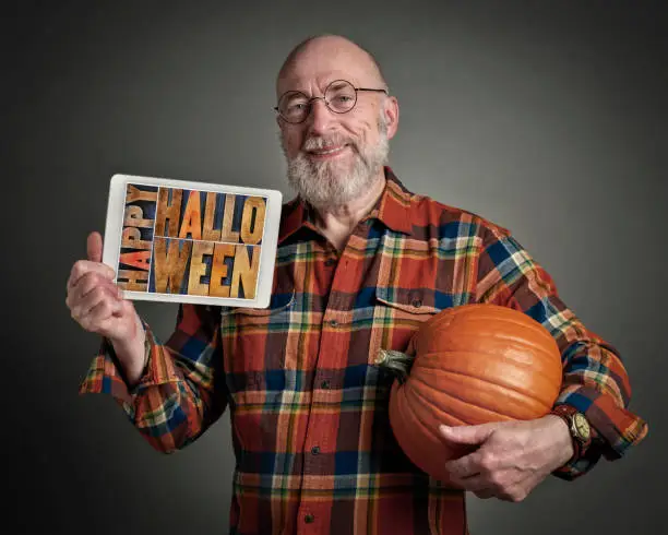 Happy Halloween - senior man with pumpkin is holding a digital tablet with sign in letterpress wood type