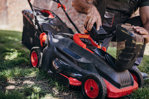 Senior man putting battery into electric cordless lawn mower
