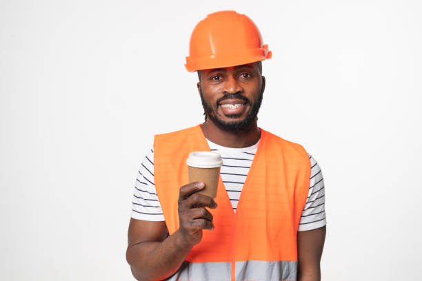 istock African-american young man construction worker engineer architect in reflective orange vest and hardhat drinking coffee hot drink isolated in white background 1405424115