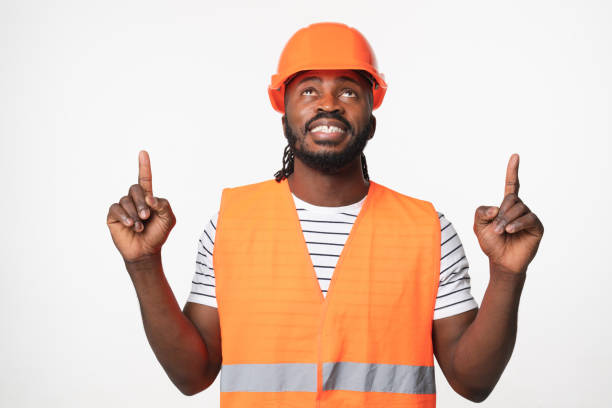 istock Young african-american man construction worker engineer architect in reflective orange vest and hardhat pointing at copy space upwards isolated in white background 1405424148