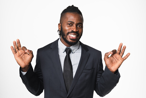 Cheerful african-american young businessman ceo leader boss freelancer in formal suit showing okay gestures smiling with toothy smile isolated in white background