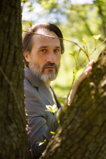 istock Mature grey beard businessman wearing casual grey jacket looking thru tree trunks leaning on one. Life after 40 years concept, problems and depression. Middle age crisis 1405428554