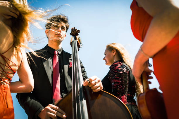 Three musicians in red dress and one musician in black suit at the beach. Three musicians in red dress and one musician in black suit at the beach. Music group playing violin, flute and double bass. Album cover. contra bassoon stock pictures, royalty-free photos & images