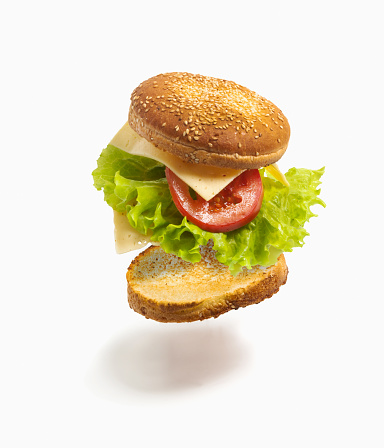 Flying deconstructed sandwich made from slices of bread, tomato, cheese and green lettuce on a white background. Levitation of a simple sandwich. Isolated.