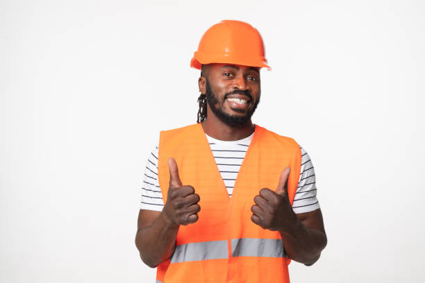 istock Happy african-american young man engineer construction worker architect in orange reflective vest and hardhat looking at camera showing thumb up isolated in white background 1405430811