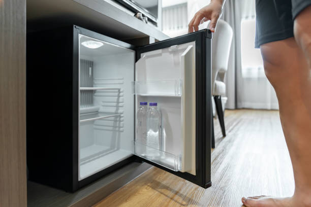 istock Man Hand opened mini small refrigerator and reached drinking plastic water bottle under the wood counter in the hotel resort bedroom. 1405430812