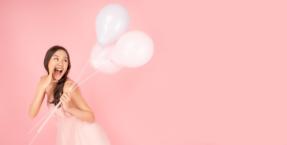 Surprised happy pretty asian woman looking to copy space in excitement holding balloons Expressive facial expressions Presenting product Beautiful girl act like a telling something Pink background