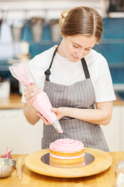 美味しいケーキを作る女性パティシエ。パン屋の回転ケーキスタンドに置かれたスポンジ層にパイピングバッグからピンククリームを入れた女性 - cake women confectioner photography ストックフォトと画像