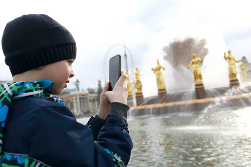 Child takes photo of fountain with smartphone in park