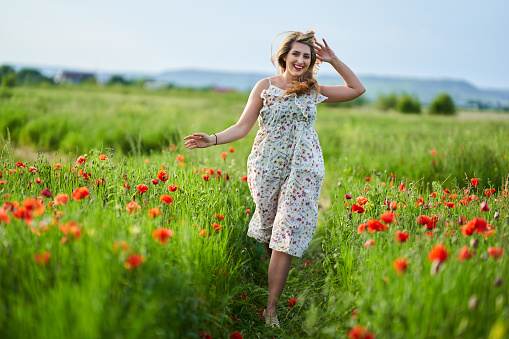 Beautiful plus size young indian woman in floral dress in a poppy field