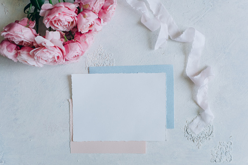 Flay lay of an envelope in between scattered lisianthus flowers and a pink book against a pastel pink background.