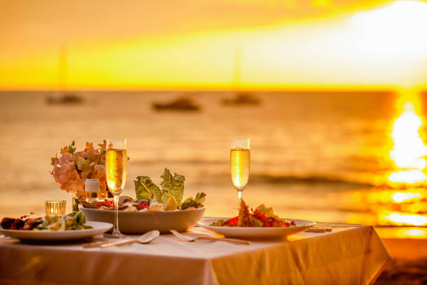 해변에서 낭만적 인 일몰 저녁 식사. 테이블 신혼 여행은 바다가 보이는 레스토랑에서 고급스러운 음식, 샴페인 음료 한 잔으로 두 명을위한 것입니다. 여름 사랑, 휴가 개념의 로맨스 데이트 - honeymoon color image horizontal setting the table 뉴스 사진 이미지