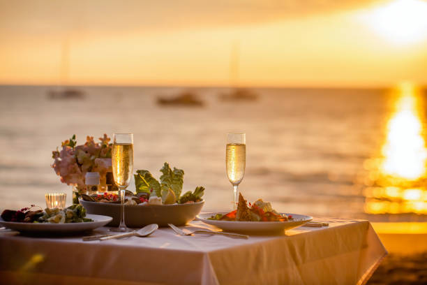 romantic sunset dinner on the beach. table set for two with luxurious food, glasses of champaign drinks in a restaurant with sea view. summer love, romance date concept - restaurant wine table table for two imagens e fotografias de stock