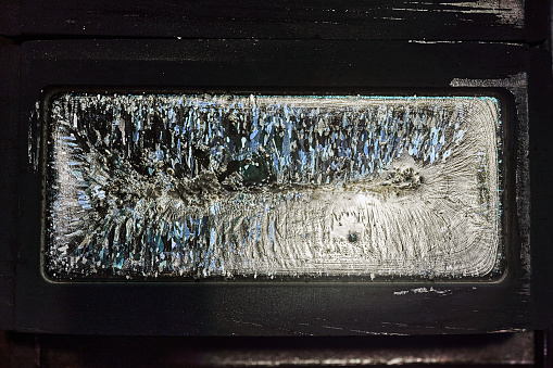 An ingot of silver lies in a graphite mold. Shoot vertically from top to bottom. The crystal structure of the solidified metal is clearly visible.