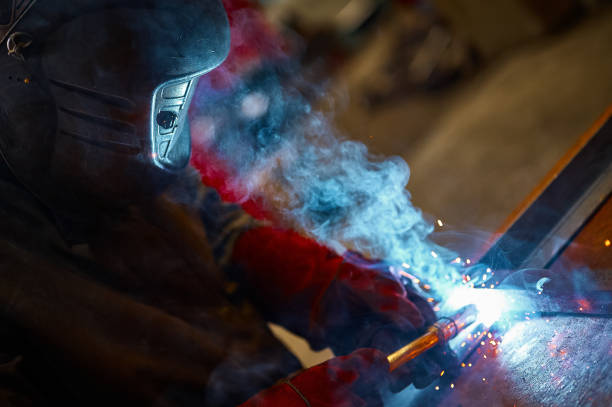 A bustling street market workshop where a worker welds metal, sending bright sparks as vendors and passersby observe the activity and repair work amid an urban, cobblestone setting.