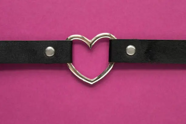 Black leather choker with metal heart on fuchsia color background