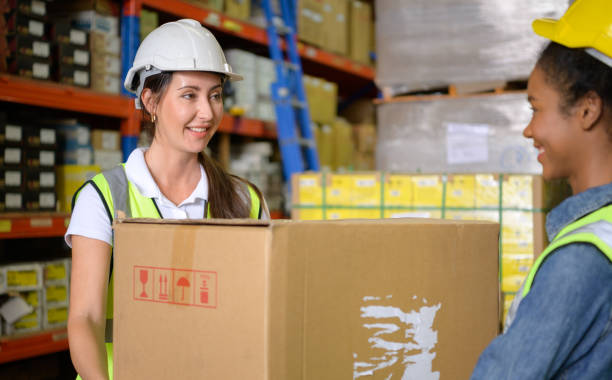 istock Two girls warehouse workers Help each other lift heavy boxes to move storage. 1405439862