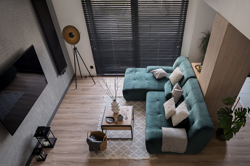 Top view on small and stylish living room with big window with black blinds, cozy sofa, tv, coffee table and decorations