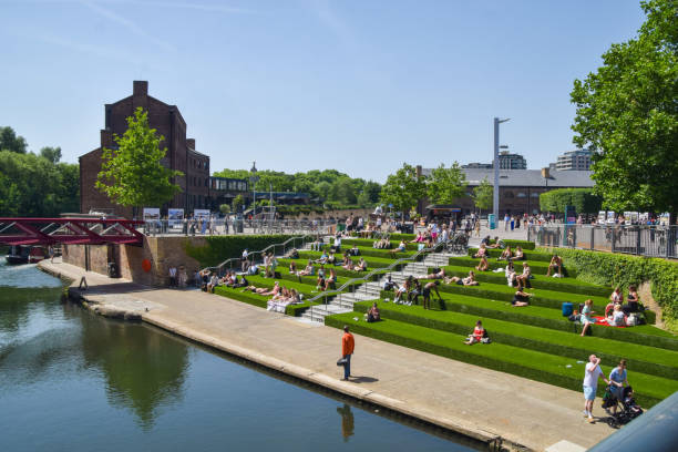 la gente disfruta del sol en los verdes escalones de césped artificial en granary square, king's cross. - estación de kings cross fotografías e imágenes de stock